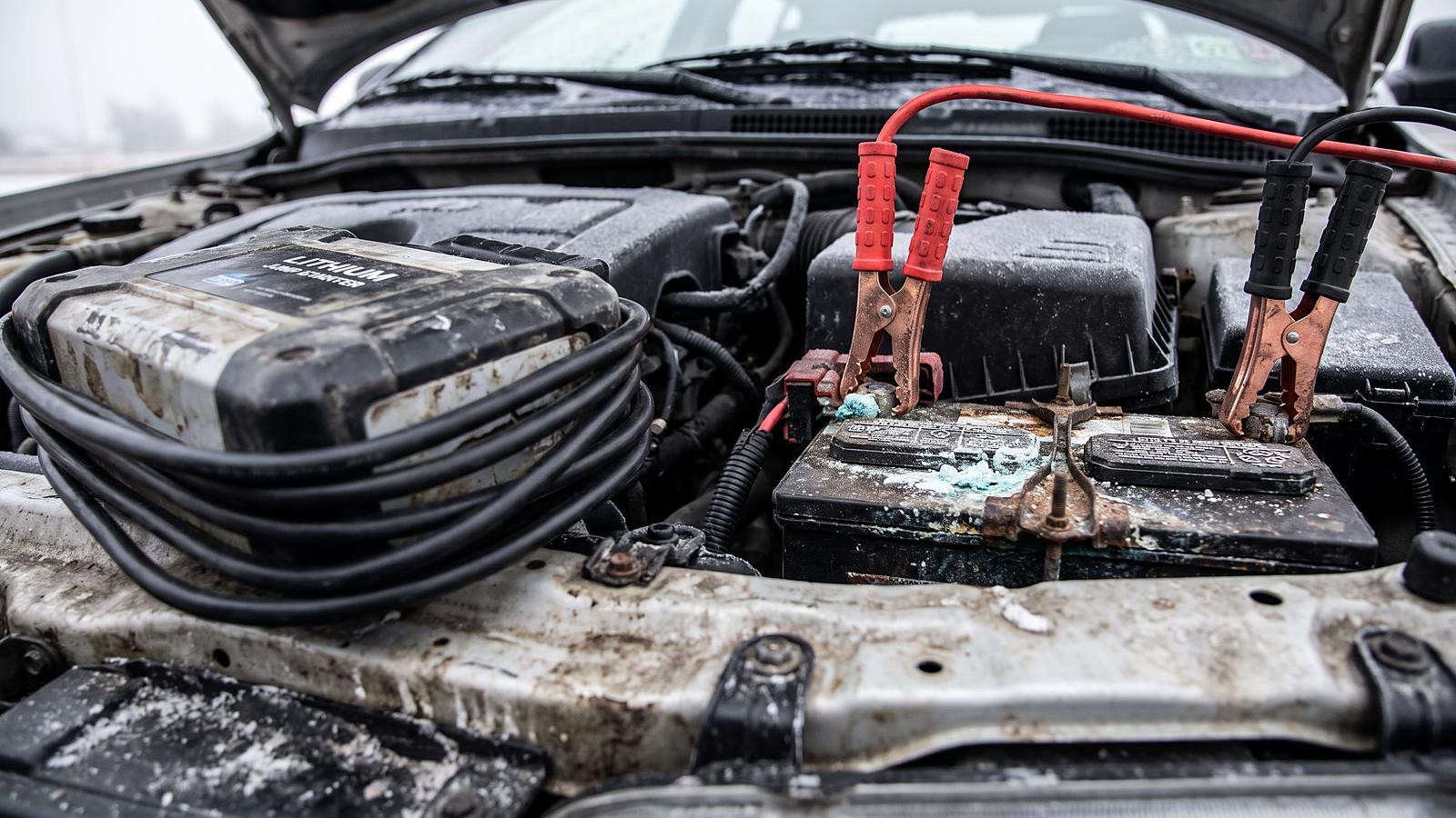 Red and black jumper cable clamps on a car battery terminal under an open hood on a cold morning